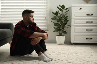 Photo of Sad man sitting on floor at home. Space for text