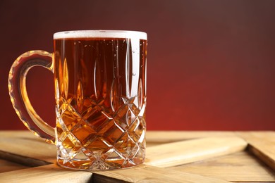 Photo of Mug with fresh beer on wooden crate against color background, closeup. Space for text