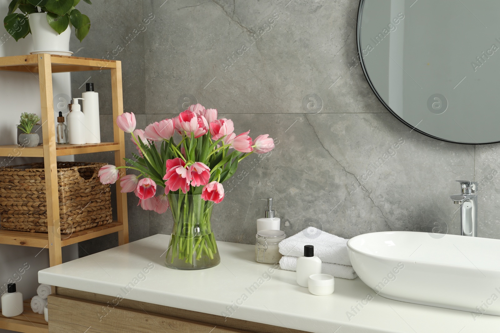 Photo of Vase with beautiful pink tulips and toiletries near sink in bathroom