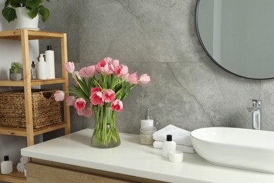 Vase with beautiful pink tulips and toiletries near sink in bathroom