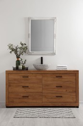 Modern bathroom interior with stylish mirror, eucalyptus branches, vessel sink and wooden vanity