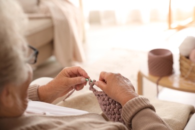 Elderly woman crocheting at home, closeup. Creative hobby