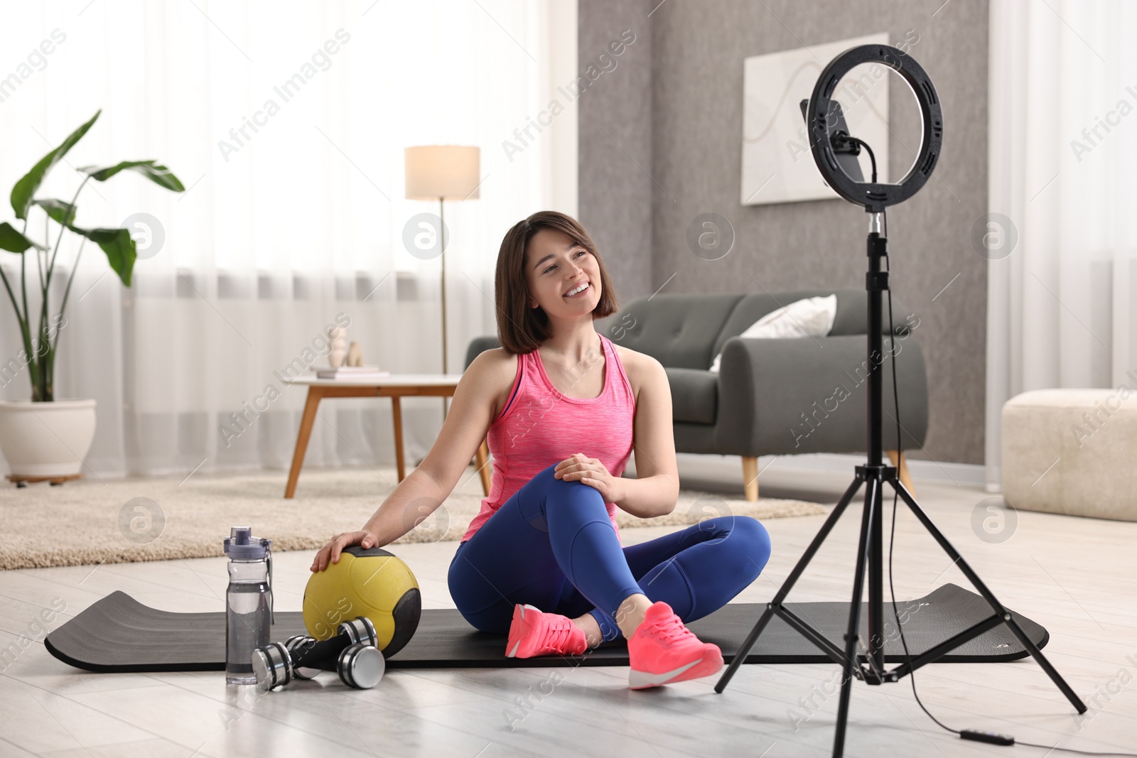 Photo of Happy sports blogger with medicine ball while streaming online fitness lesson with smartphone at home