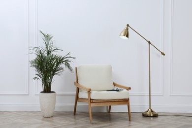 Photo of Stylish room interior with lamp, armchair and houseplant near white wall