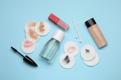 Photo of Bottle of makeup remover, dirty cotton pads, buds and different cosmetic products on light blue background, flat lay