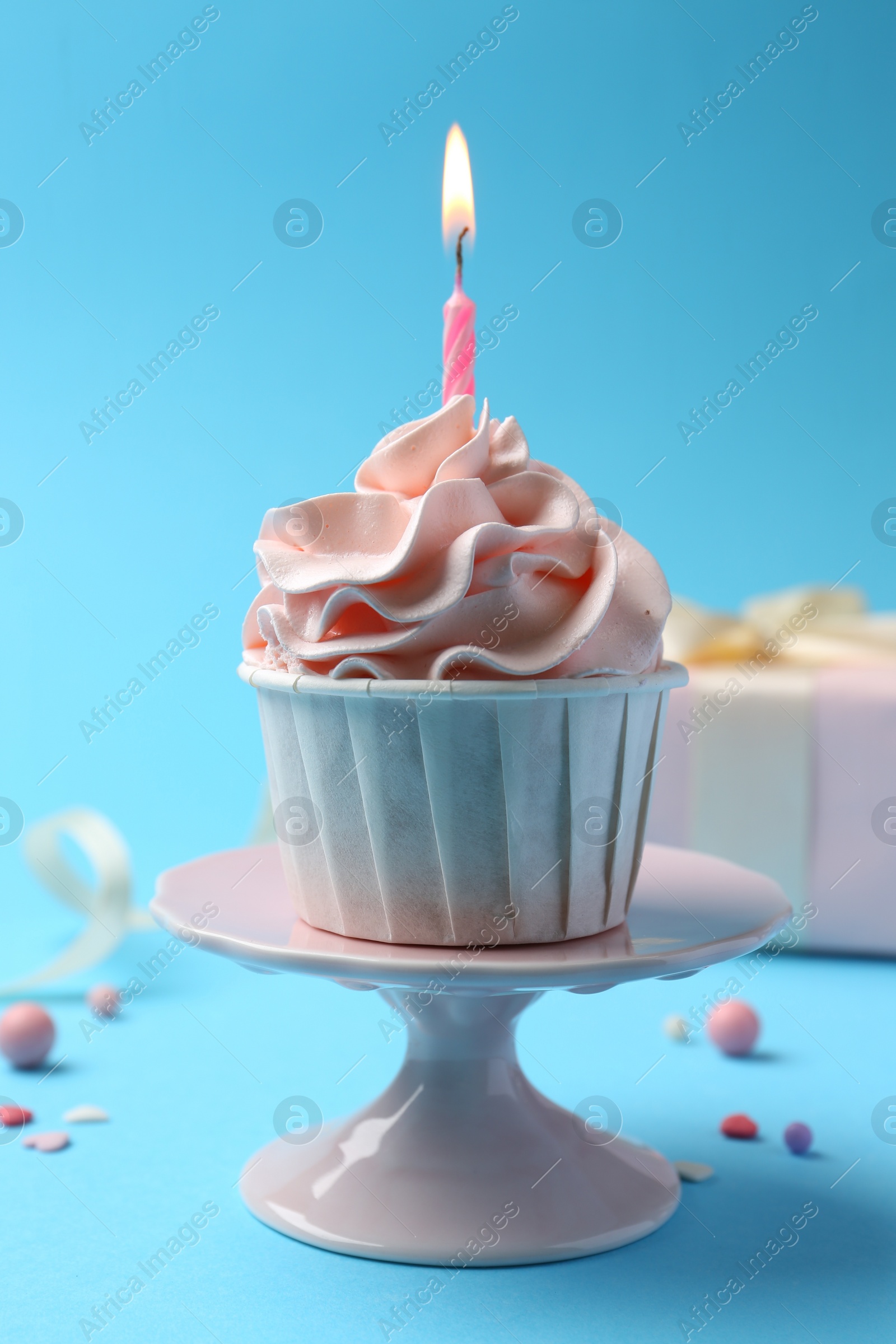 Photo of Delicious birthday cupcake with burning candle and sprinkles on light blue background, closeup