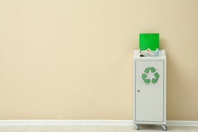 Trash bin with recycling symbol near color wall indoors. Space for text