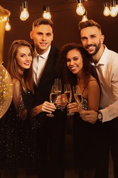 Happy friends with glasses of sparkling wine celebrating New Year indoors