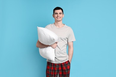 Photo of Happy man in pyjama holding pillow on light blue background