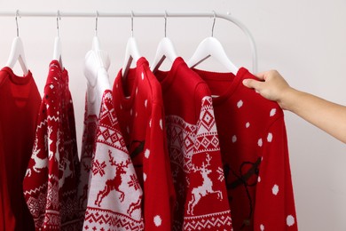 Photo of Woman choosing Christmas sweater from rack near white wall, closeup
