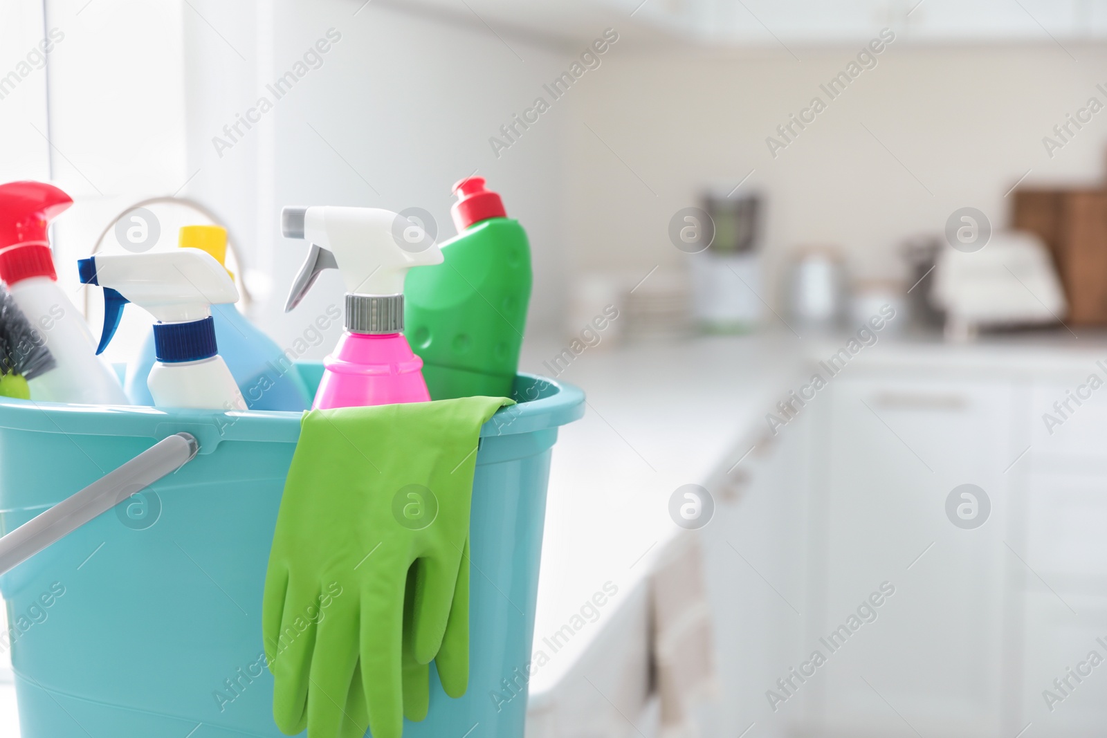 Photo of Plastic bucket with different cleaning supplies in kitchen, closeup. Space for text