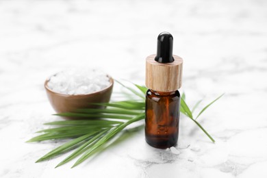 Photo of Bottle of essential oil, sea salt and green twig on white marble table, closeup