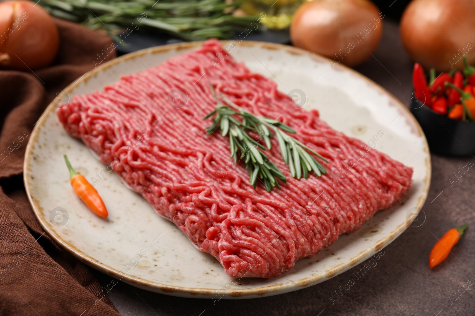 Photo of Fresh raw ground meat, chili peppers and rosemary on brown table, closeup