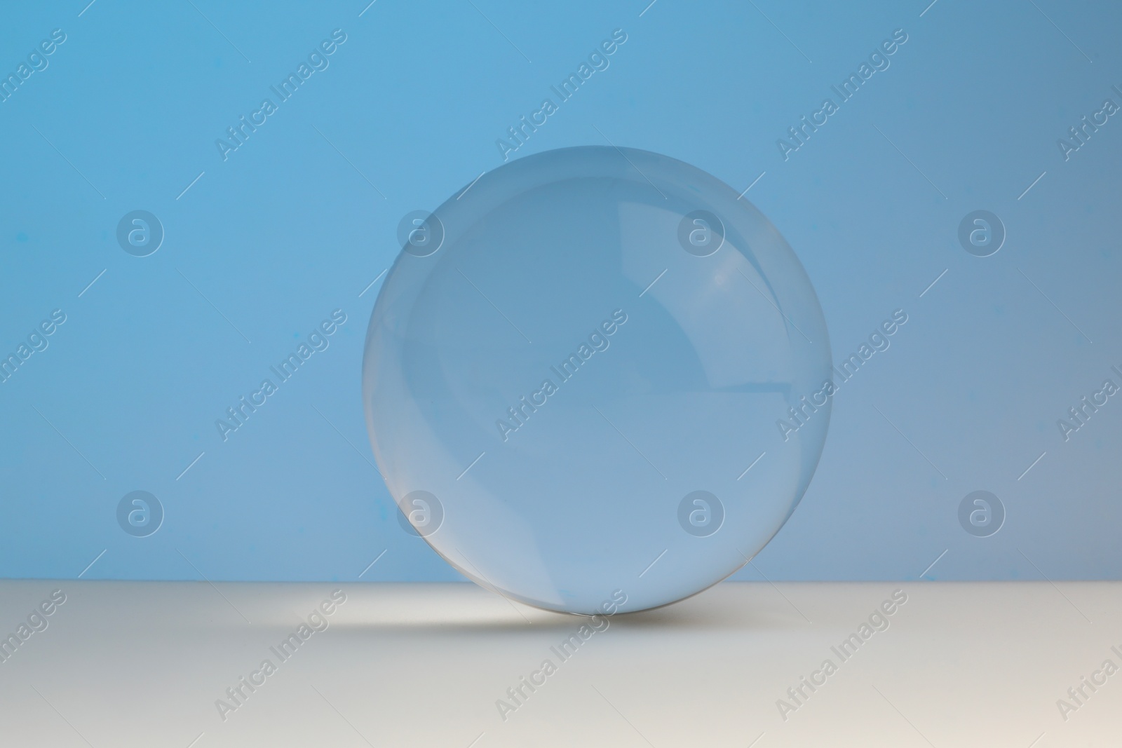 Photo of Transparent glass ball on table against light blue background