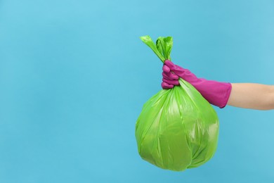 Photo of Woman holding plastic bag full of garbage on light blue background, closeup. Space for text