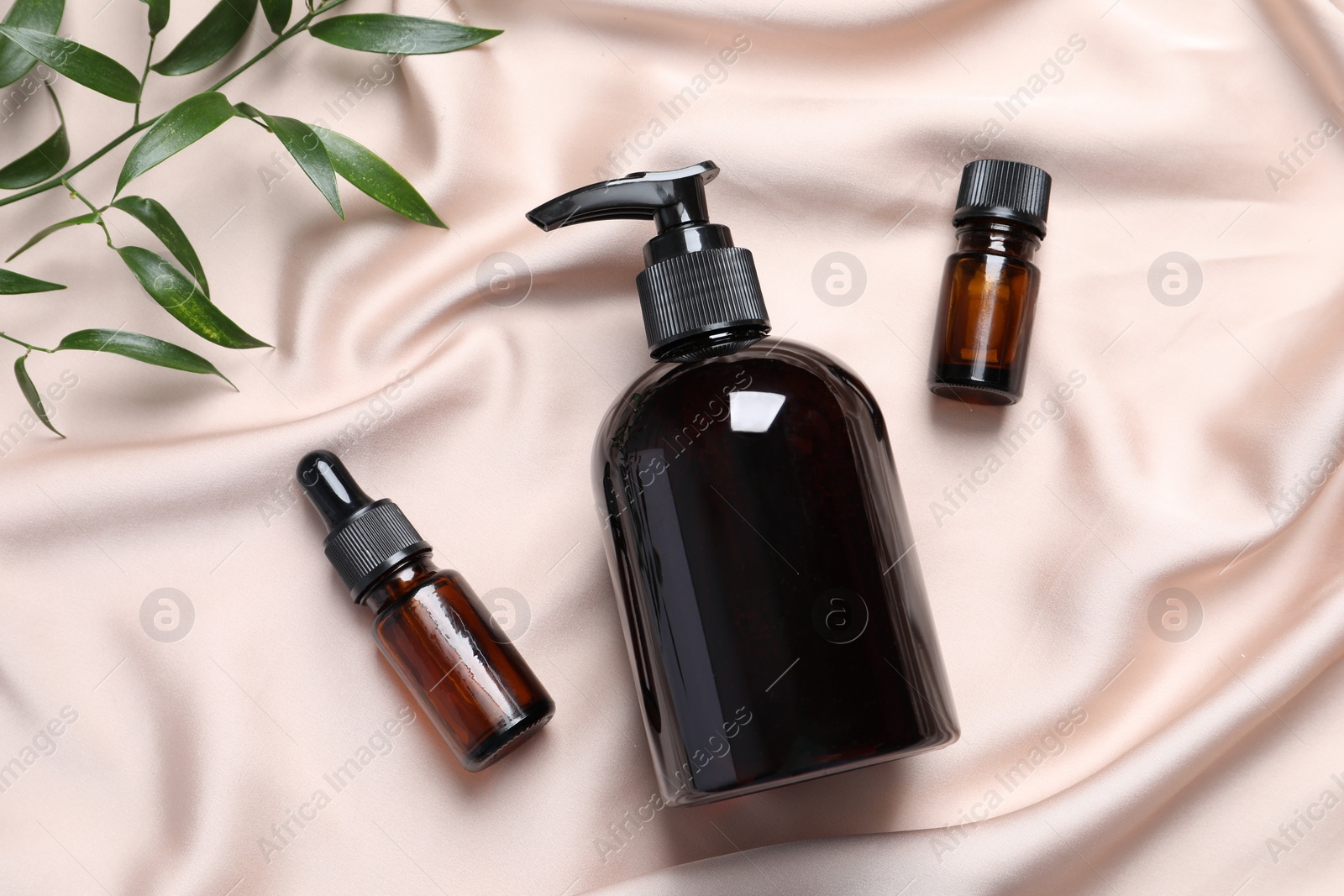 Photo of Bottle of cosmetic product and leaves on pink fabric, flat lay