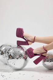 Photo of Woman in pink high heeled shoes and disco balls on white background, closeup