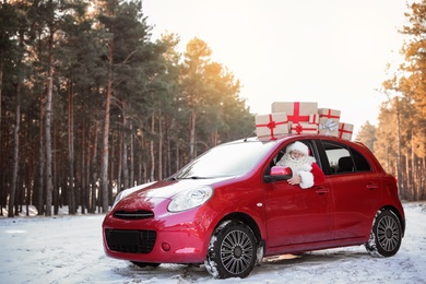 Authentic Santa Claus in red car with gift boxes, view from outside