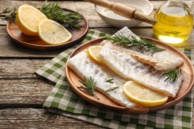 Photo of Fresh raw cod fillets with rosemary and lemon on wooden table