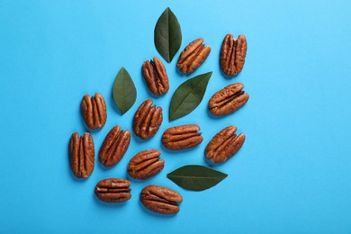 Photo of Delicious pecan nuts and green leaves on light blue background, flat lay