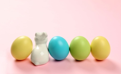 Ceramic Easter bunny and dyed eggs on color background