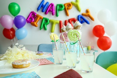 Photo of Table with treats and phrase HAPPY BIRTHDAY made of colorful balloon letters in living room