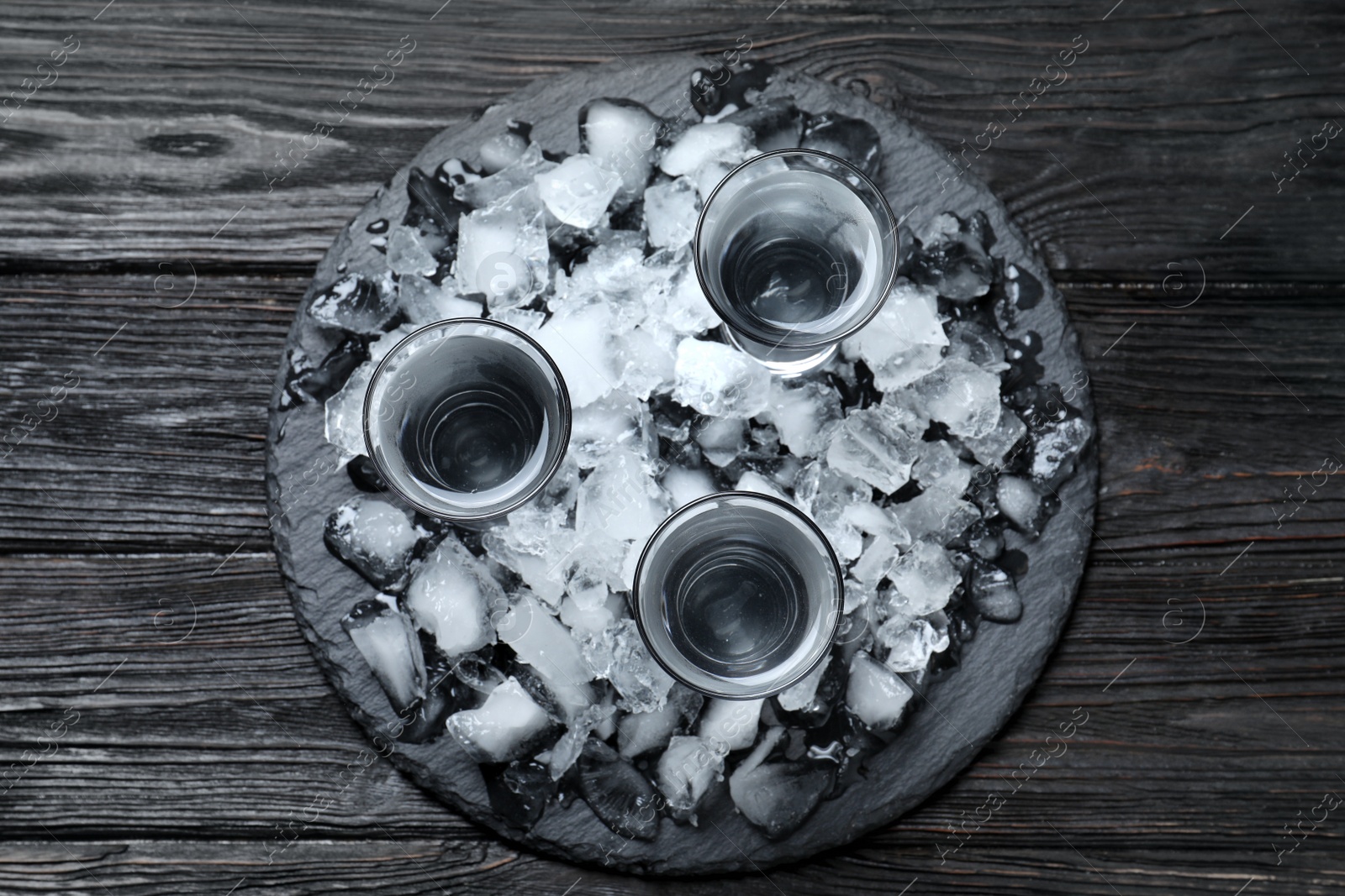 Photo of Vodka in shot glasses and ice on black wooden background, top view