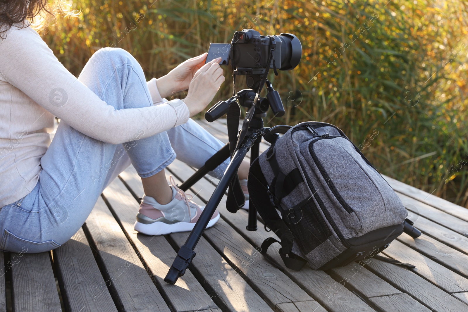 Photo of Photographer with tripod, modern camera and backpack on wooden pier