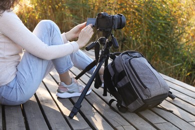 Photographer with tripod, modern camera and backpack on wooden pier