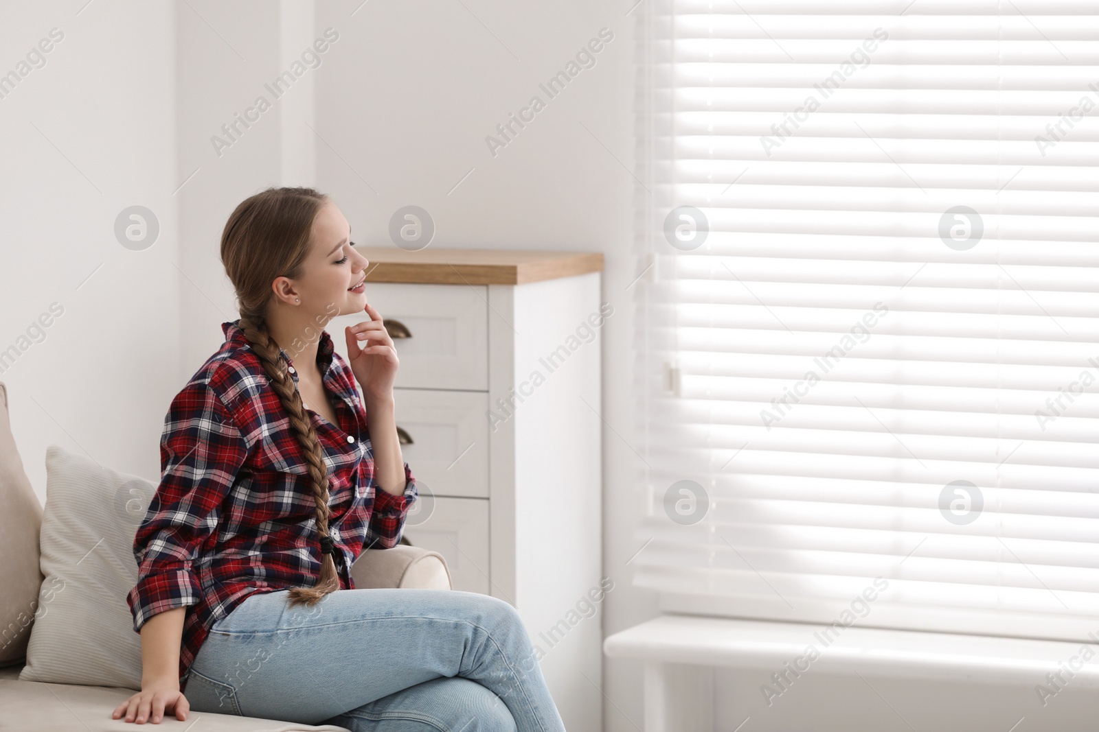Photo of Young woman sitting on sofa near window at home