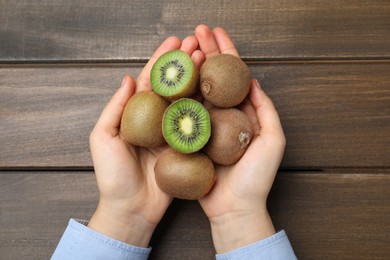 Woman holding pile of fresh ripe kiwis at wooden table, top view