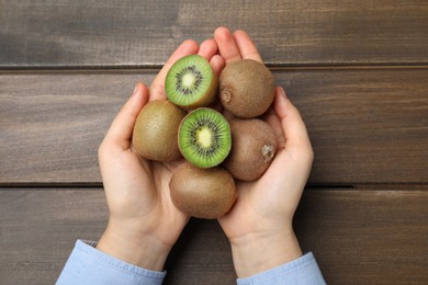 Photo of Woman holding pile of fresh ripe kiwis at wooden table, top view