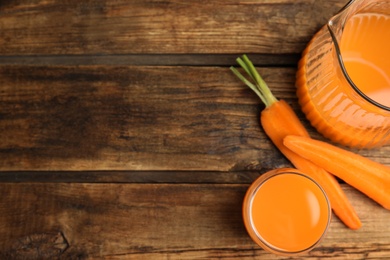 Jug and glass of freshly made carrot juice on wooden table, flat lay. Space for text