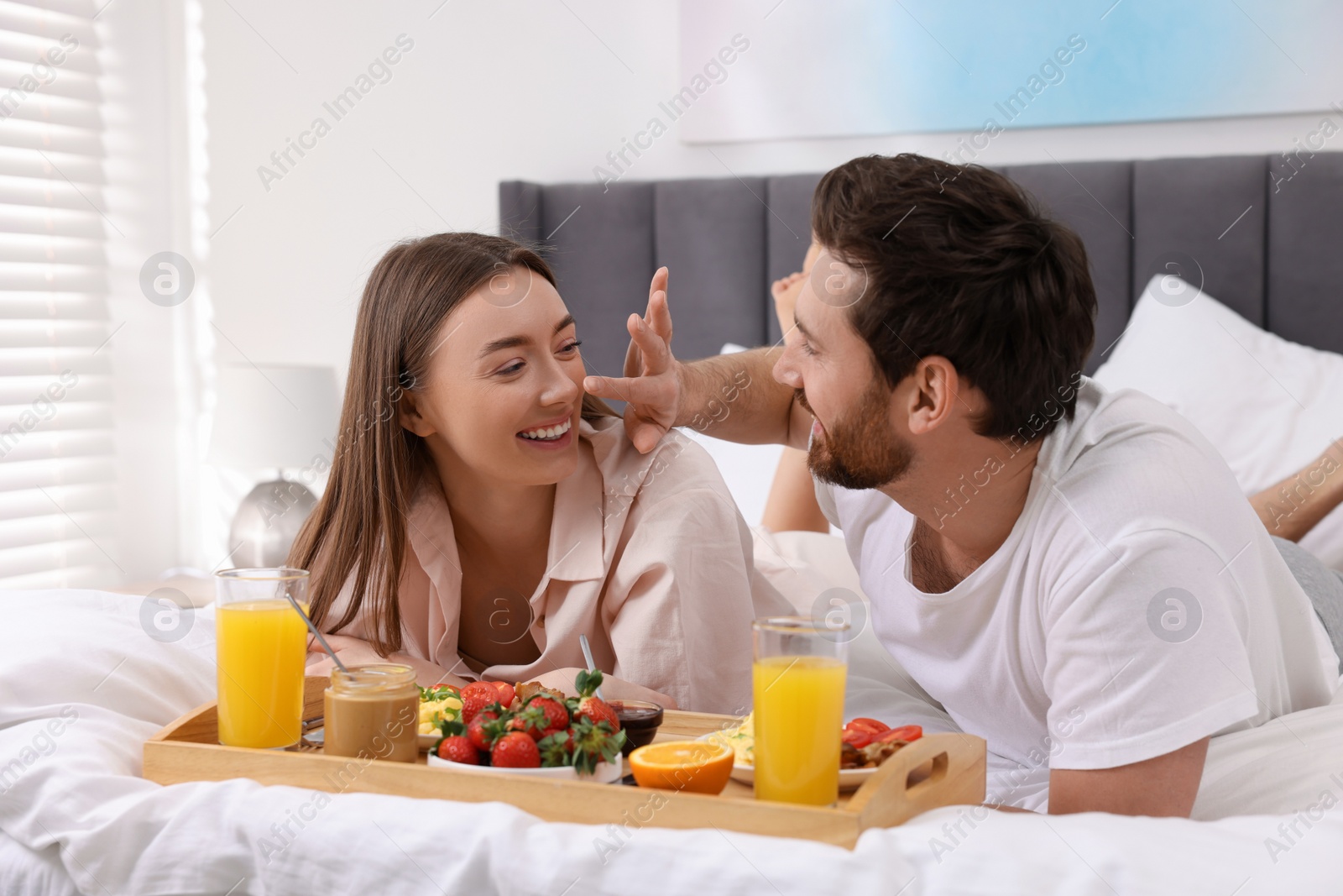 Photo of Happy couple eating tasty breakfast on bed at home