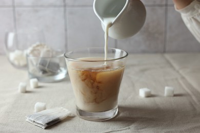 Photo of Pouring milk into cup with tea on light table, closeup