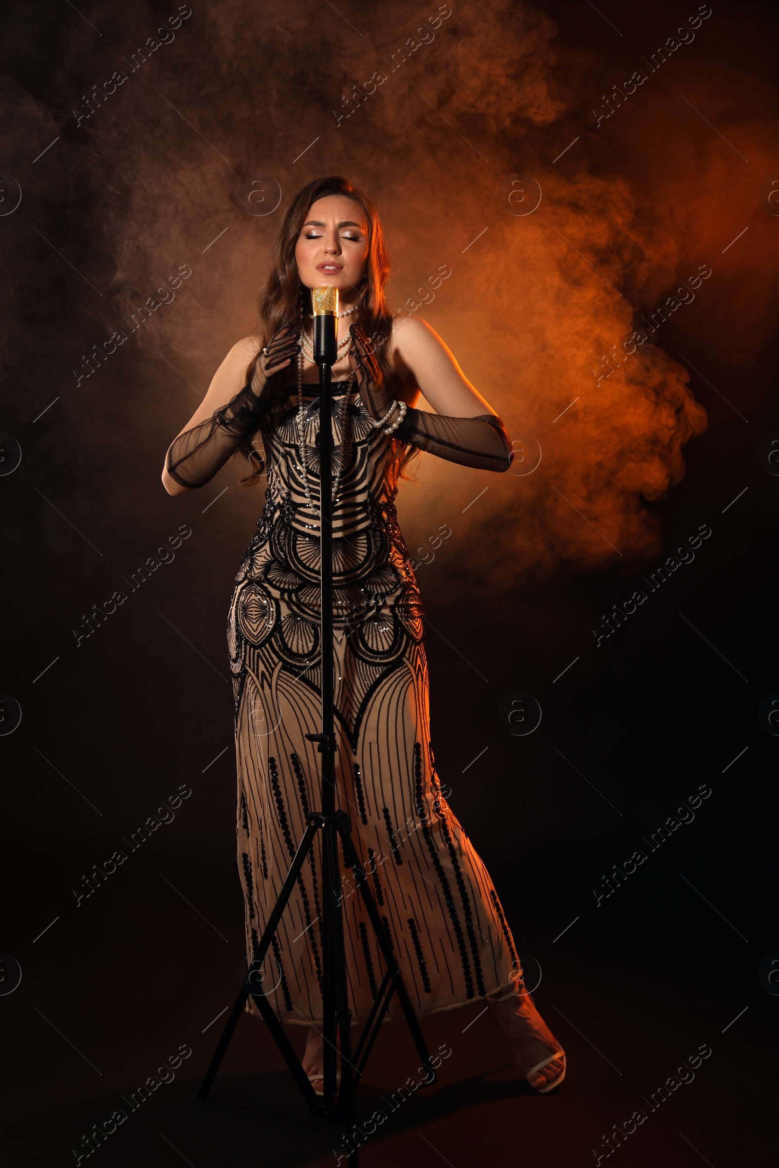 Photo of Beautiful young woman with microphone singing in color lights and smoke