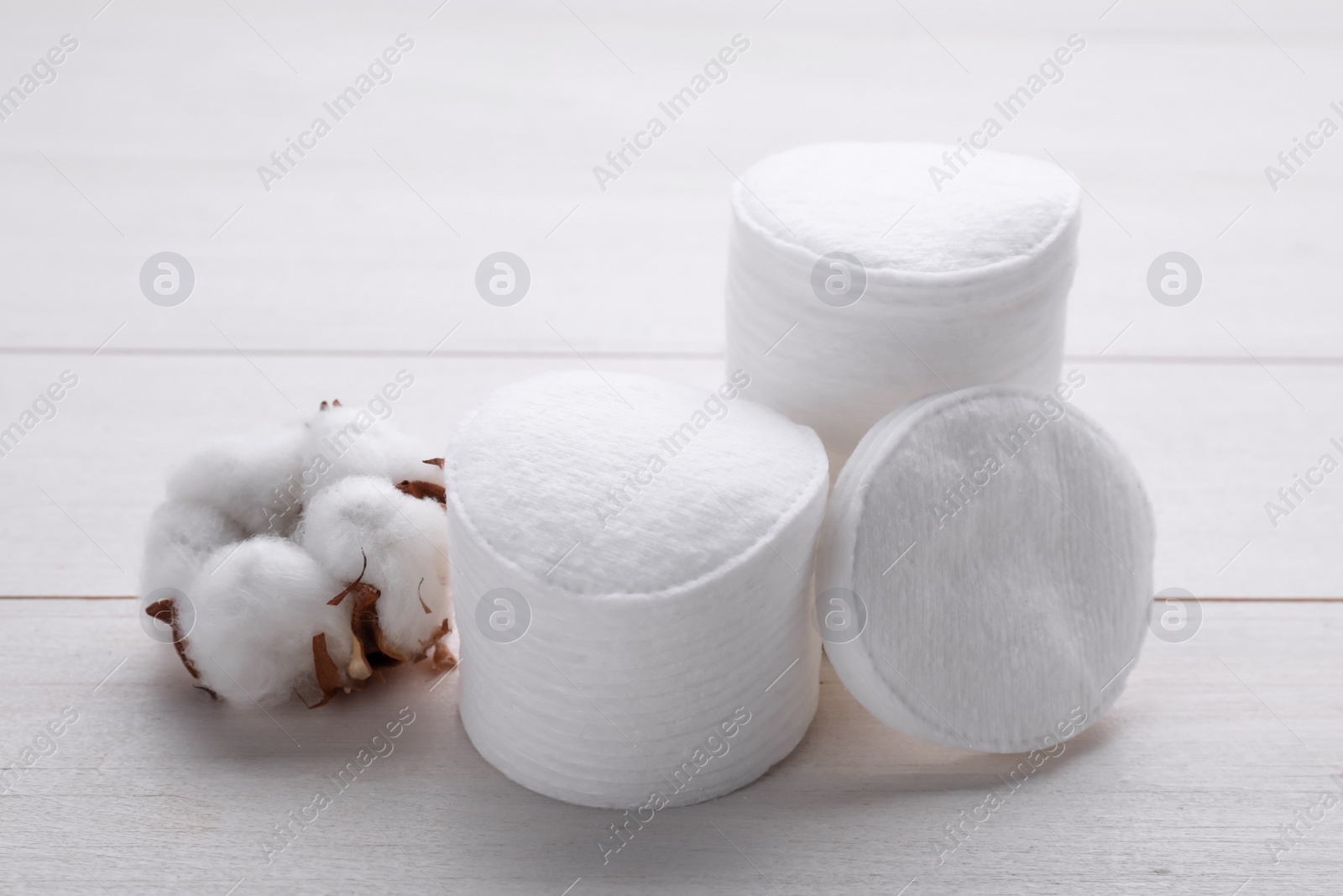 Photo of Stacks of clean cotton pads and flower on white wooden table