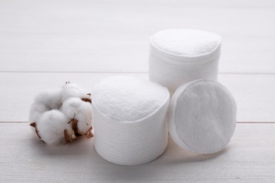 Stacks of clean cotton pads and flower on white wooden table