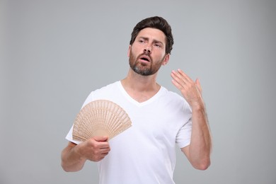 Photo of Unhappy man with hand fan suffering from heat on light grey background