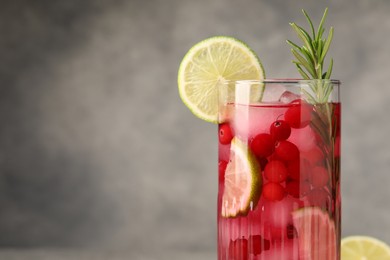 Tasty cranberry cocktail with rosemary and lime in glass on gray background, closeup. Space for text