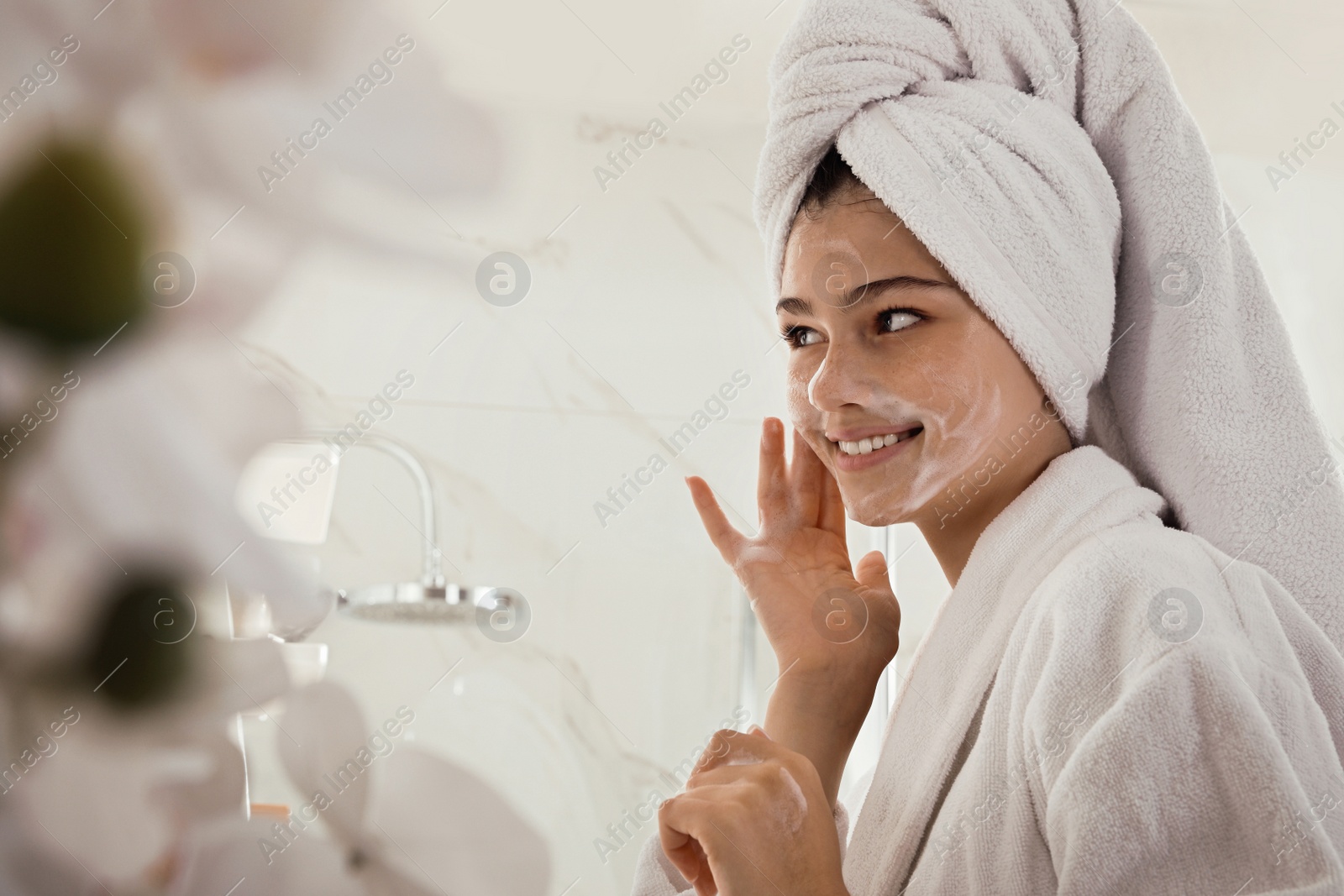 Photo of Beautiful teenage girl applying cleansing foam onto face in bathroom. Skin care cosmetic