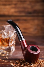 Photo of Smoking pipe with tobacco and glass of whiskey on wooden table