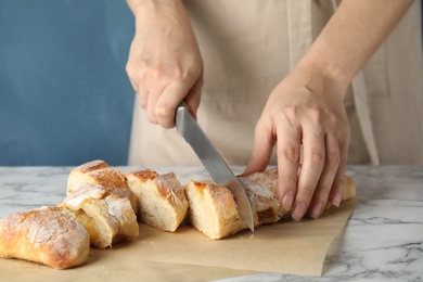 Photo of Woman cutting bread on marble table, closeup