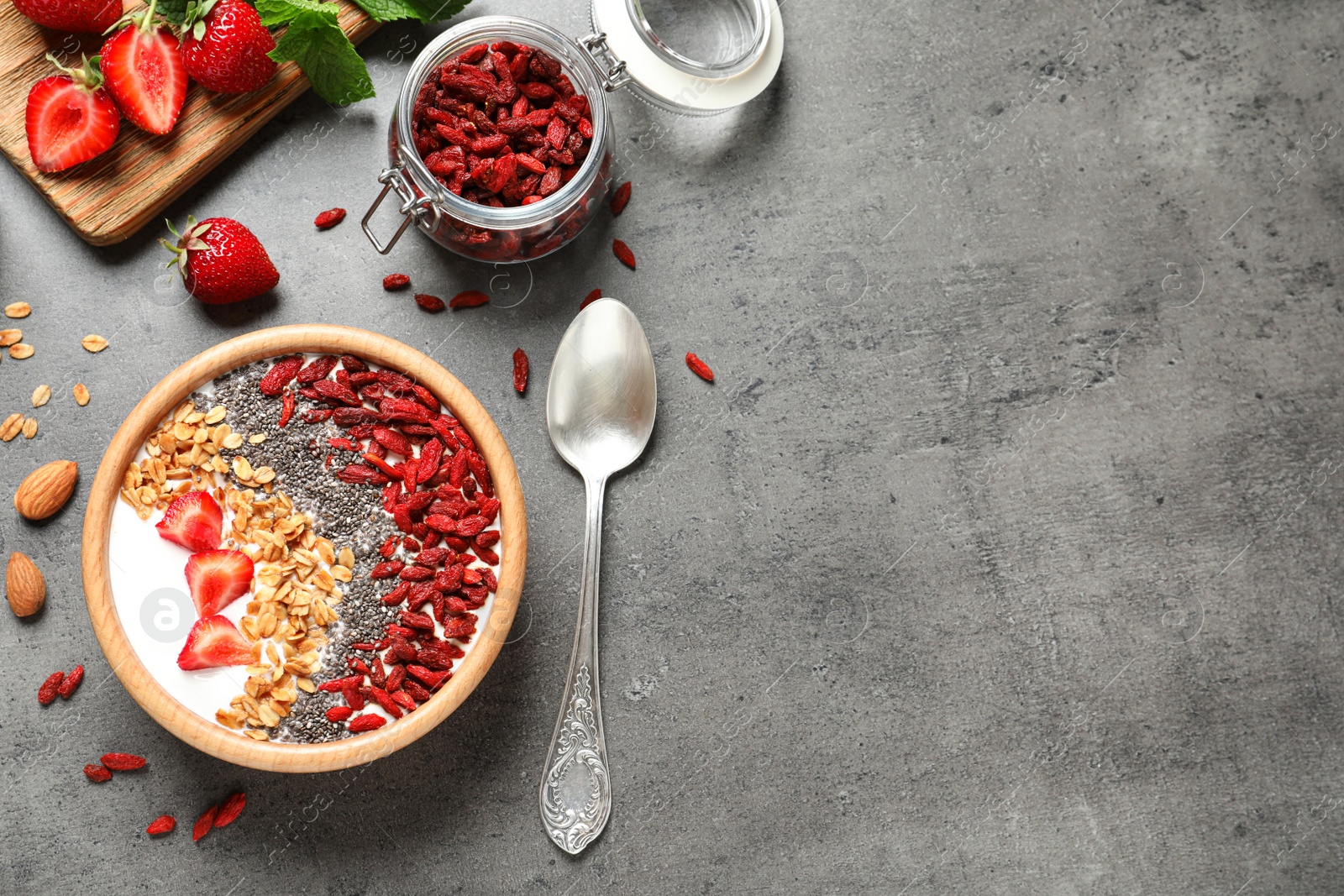 Photo of Flat lay composition of smoothie bowl with goji berries on grey table. Space for text