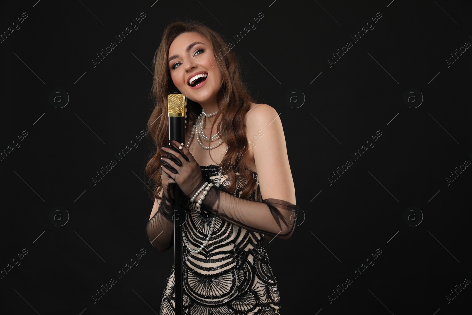 Photo of Beautiful young woman in stylish dress with microphone singing on black background