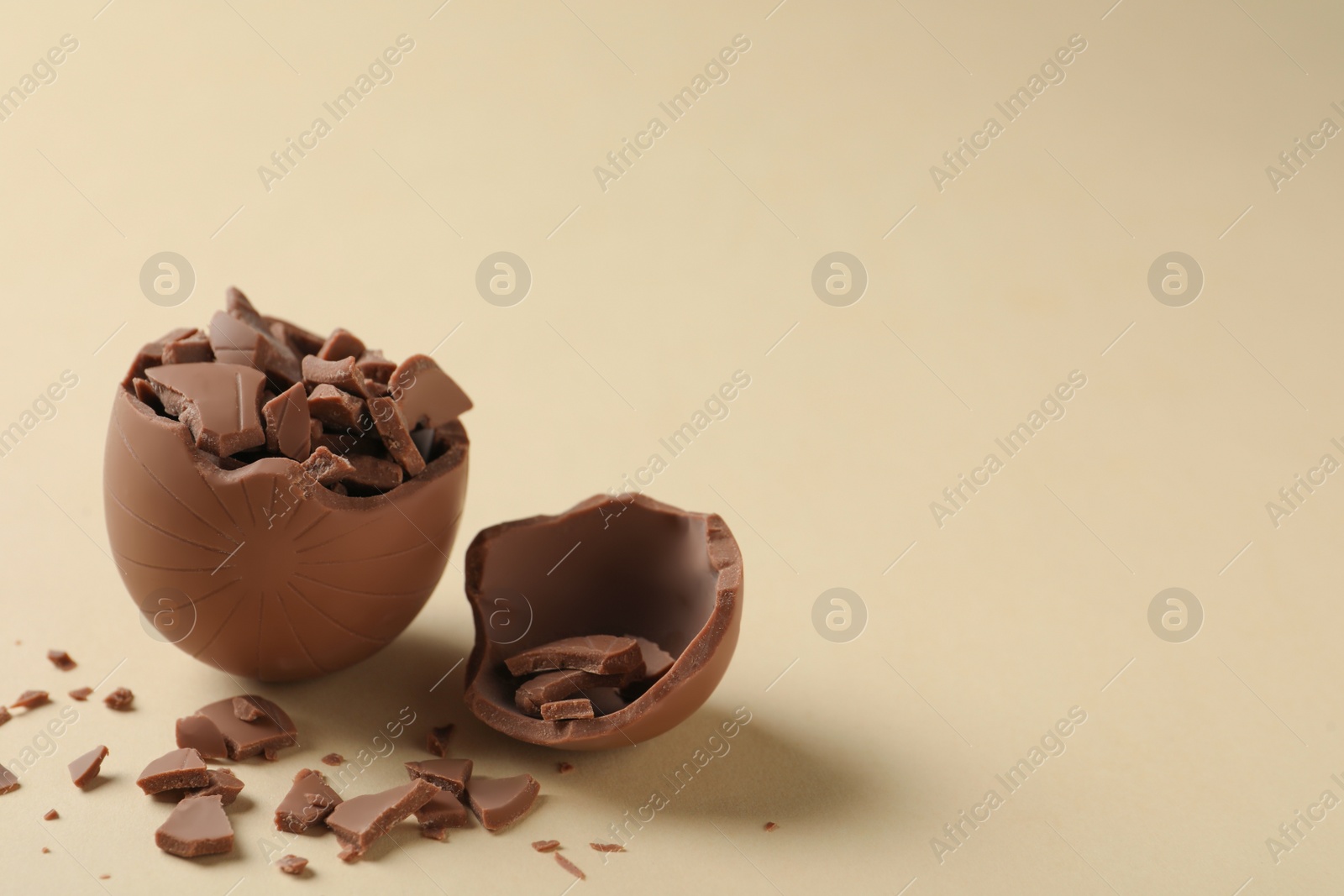 Photo of Broken chocolate egg on beige background, space for text