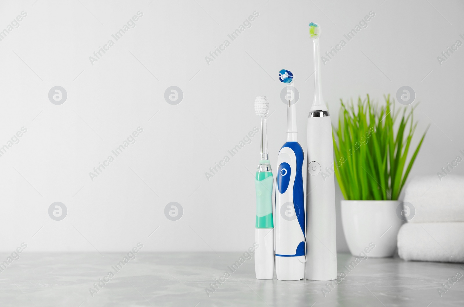 Photo of Electric toothbrushes on light grey marble table near white wall. Space for text