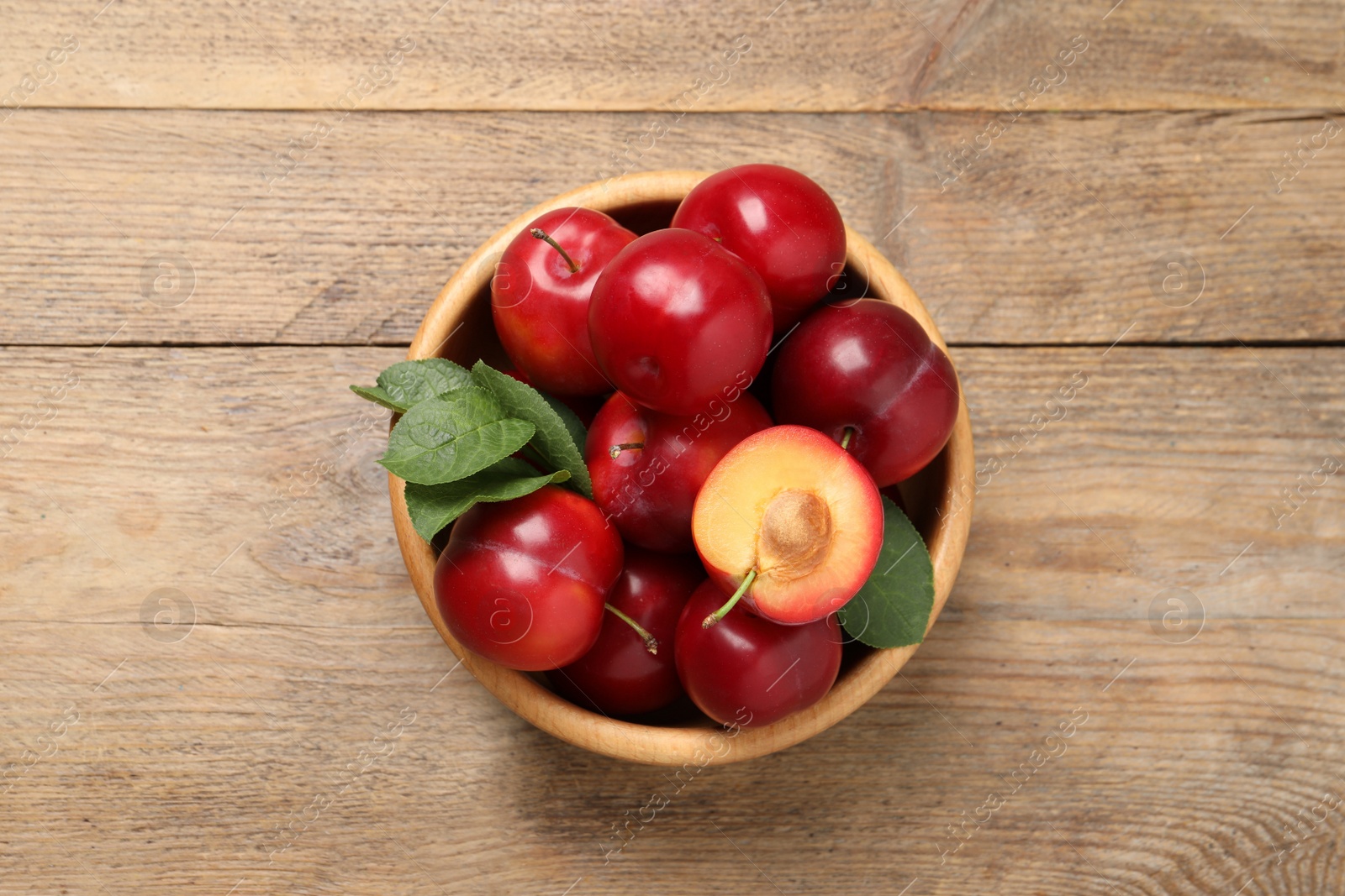Photo of Delicious ripe cherry plums with leaves on wooden table, top view