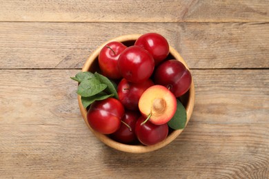 Delicious ripe cherry plums with leaves on wooden table, top view