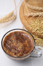 Cup of barley coffee, grains and spikes on white table, closeup